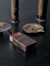 Handmade brass matchbox holder by 13 Knives shown on a dark textured surface with incense burner and burnt match