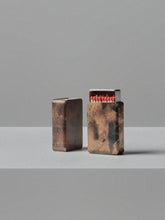 Two handmade patina brass matchbox holders by 13 Knives, one closed and one showing red-tipped matches