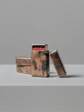 Stacked handcrafted brass matchbox holders by 13 Knives with unique flame patinas and exposed match heads