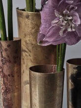 Macro detail of 13 Knives brass vases with varied patina, hammered texture, and flower stems inside each vessel
