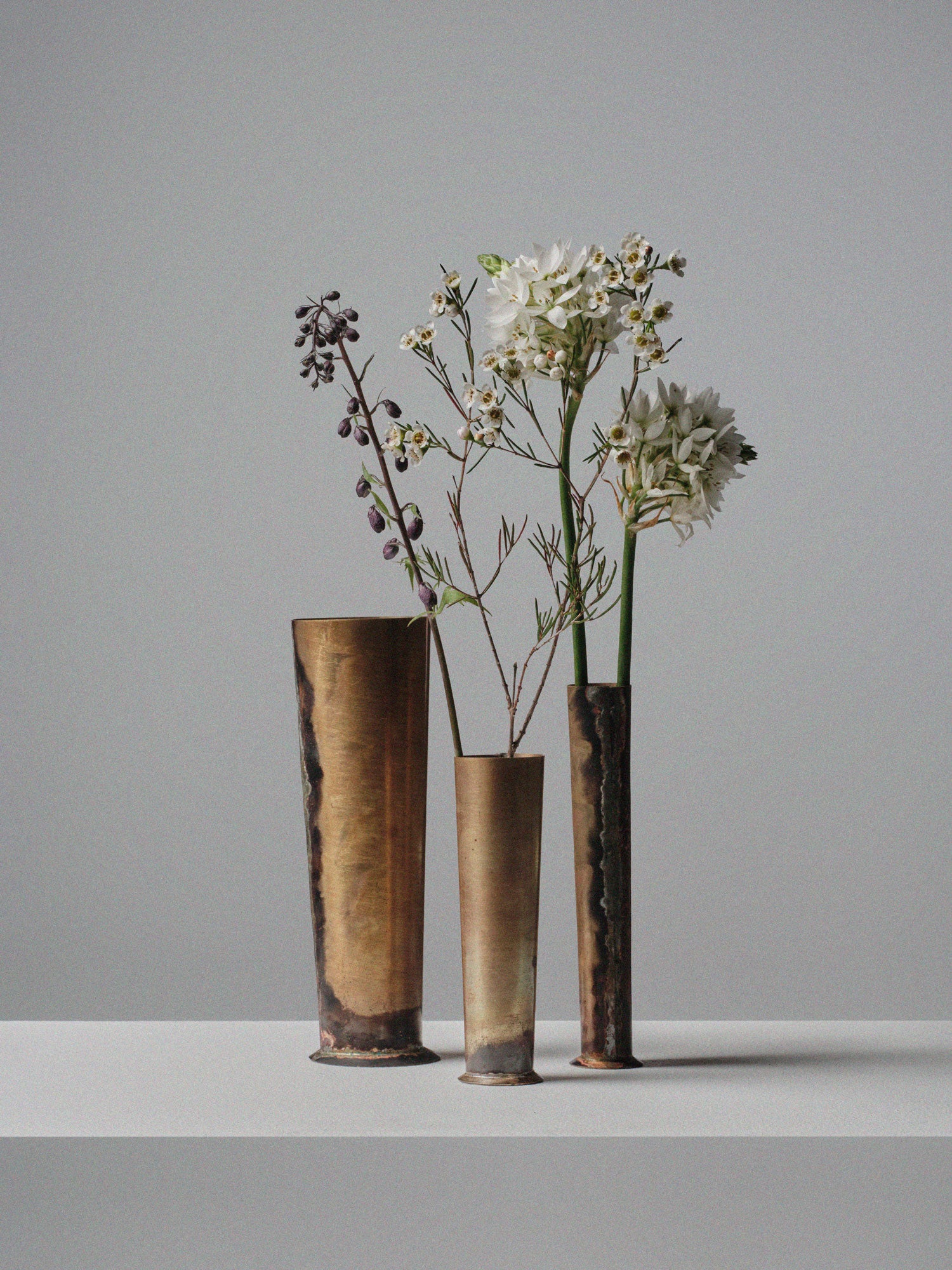 Set of three handcrafted brass vases by 13 Knives Melbourne Australia holding seasonal flowers on a minimal backdrop